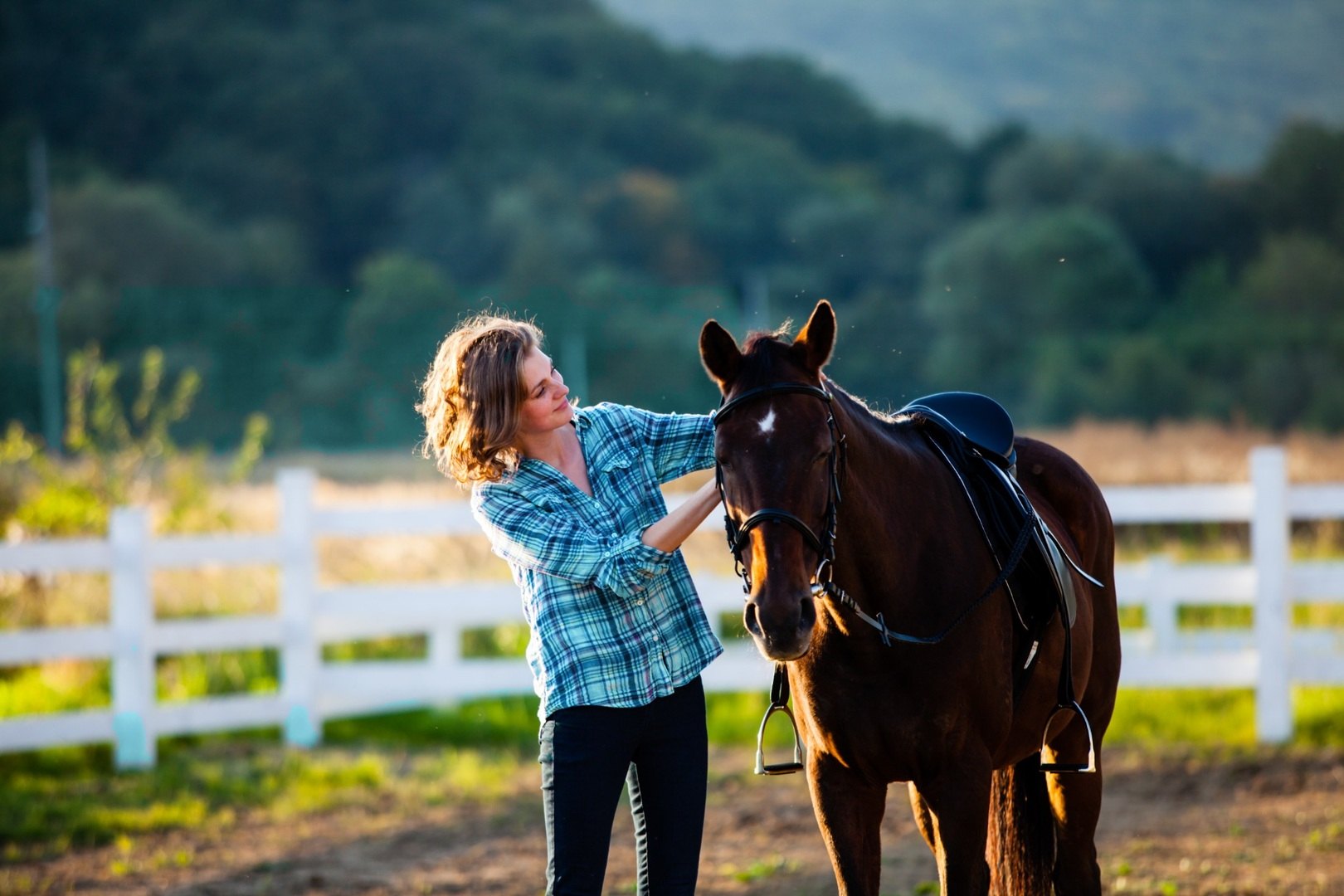Woman standing with a horse beside a white fence at golden hour